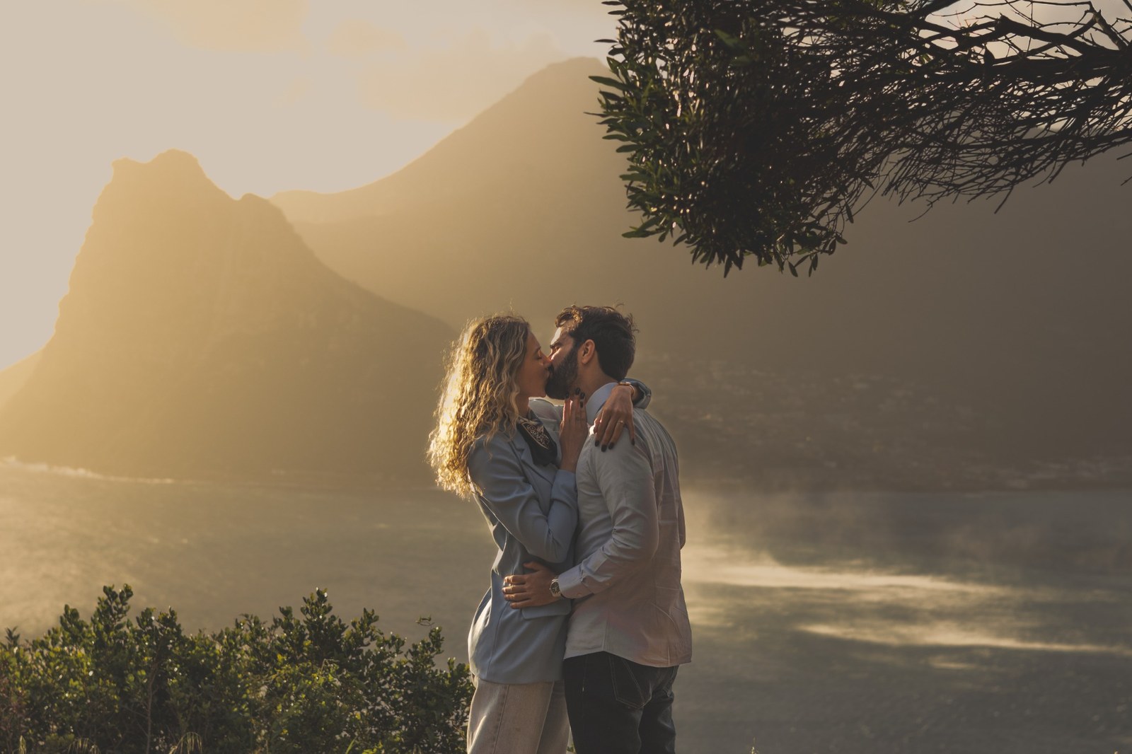 Engaged couple kissing above the golden ocean and mountains at Chapman’s Peak