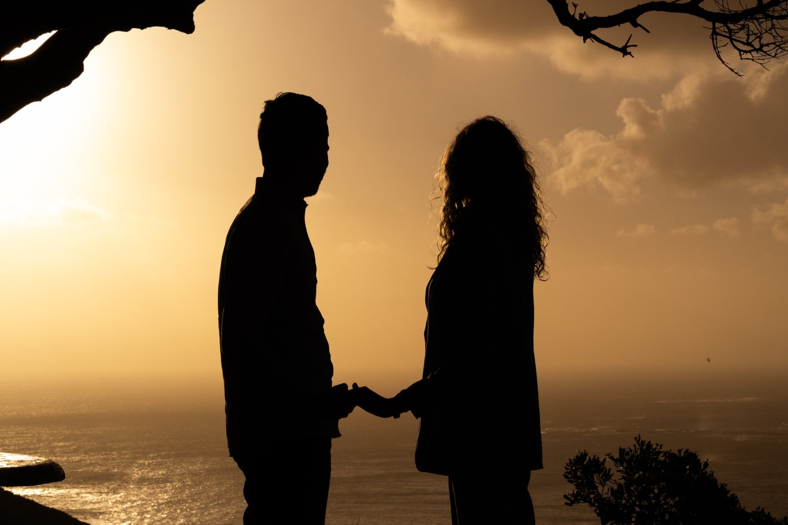 Couple holding hands in silhouette against the warm ocean light