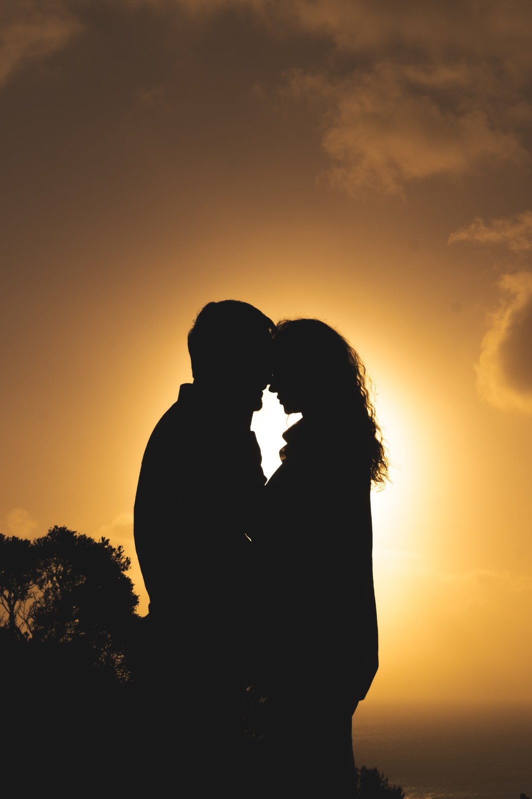 Close silhouette of the couple touching foreheads against an orange sky
