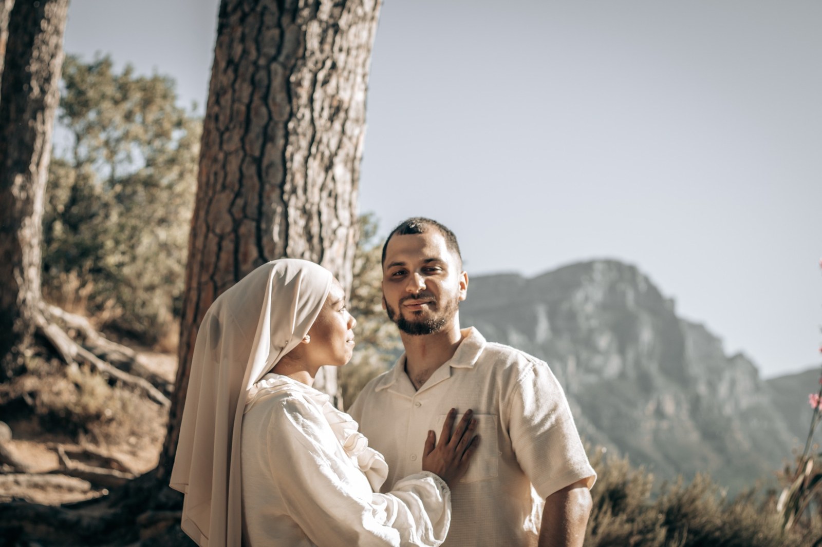 Couple standing close beside a pine trunk with the mountain behind them