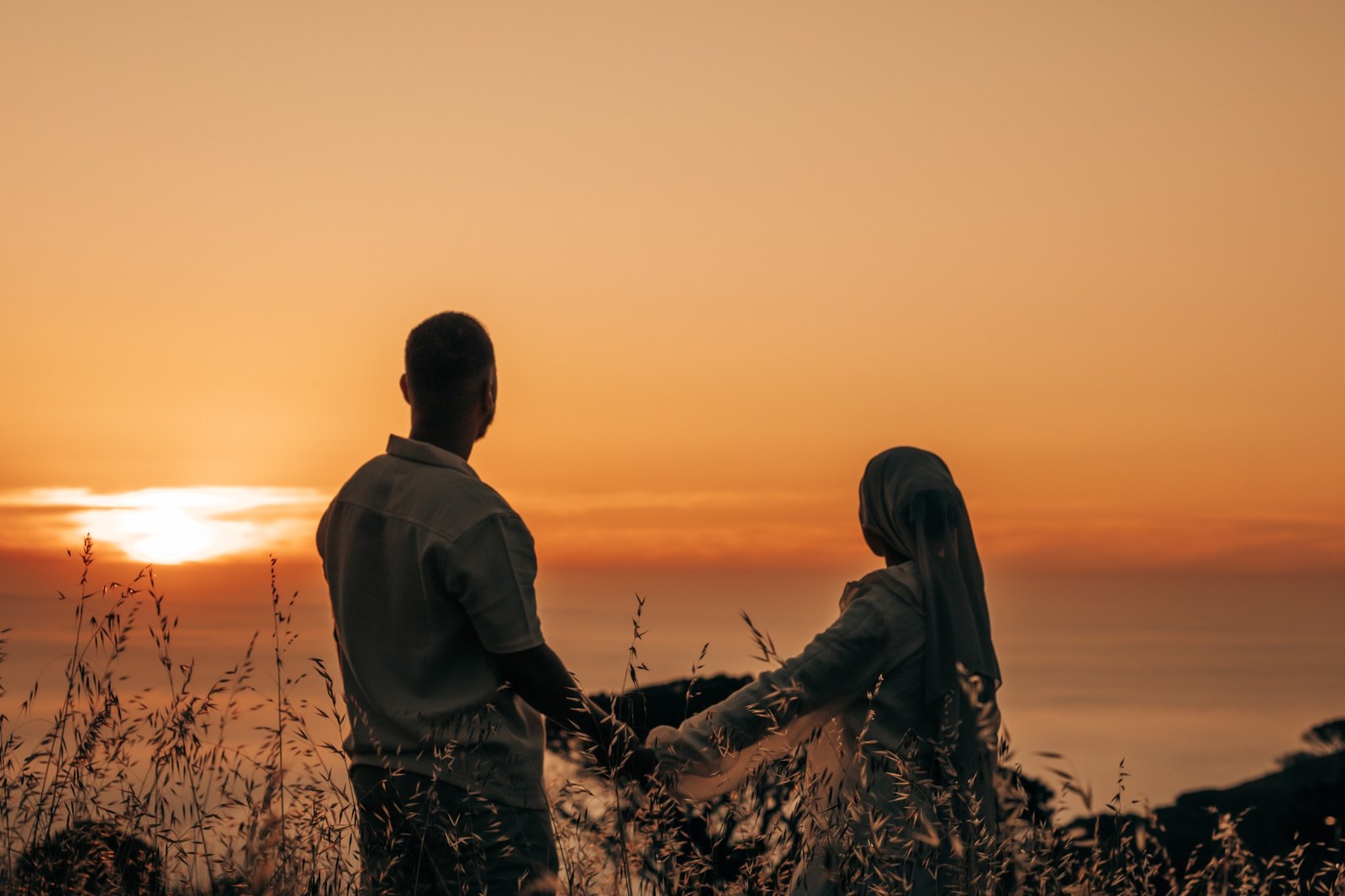 Engaged couple holding hands as they face an orange sunset