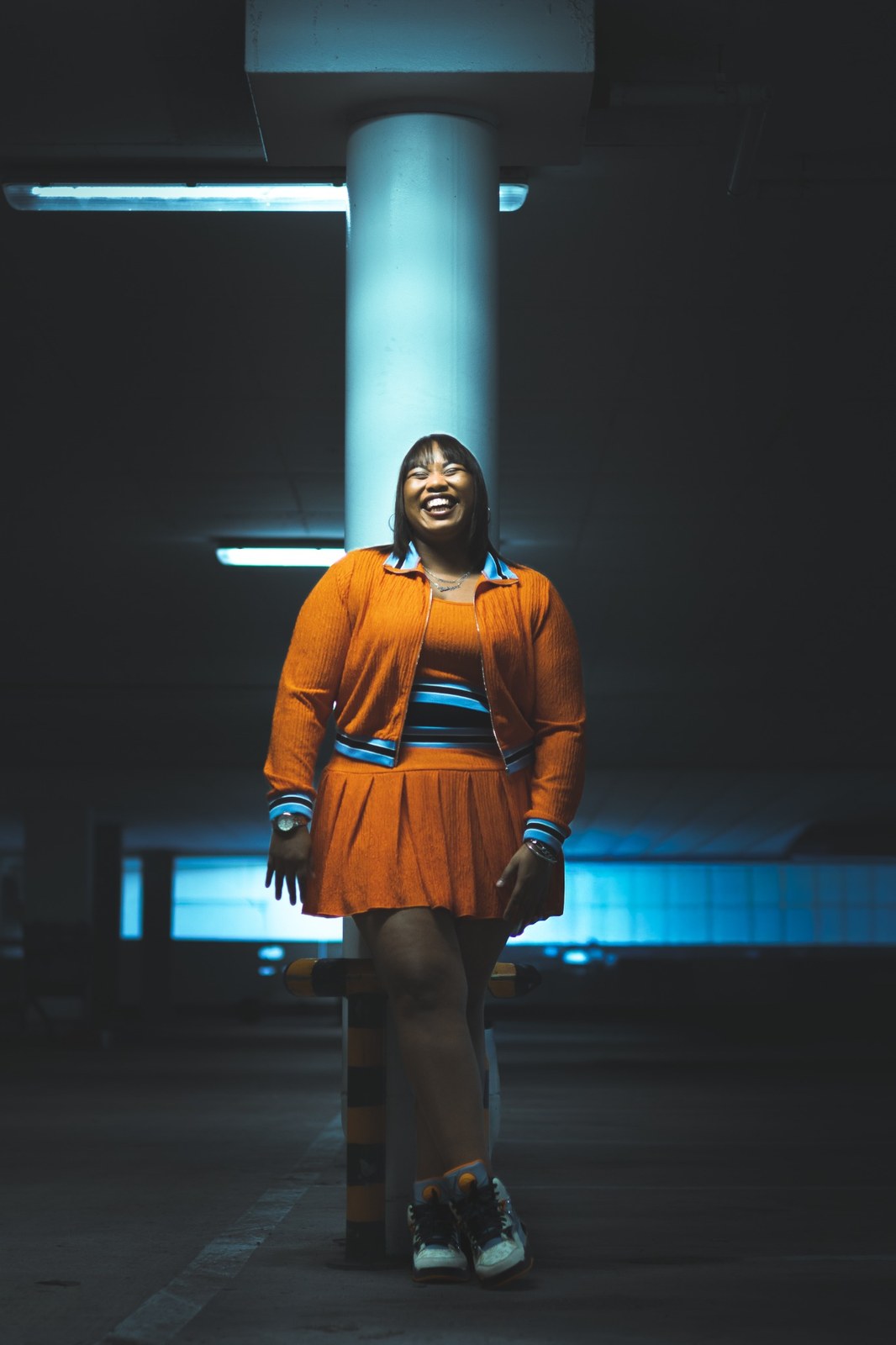 Woman smiling beneath fluorescent lights in an orange skirt and cardigan