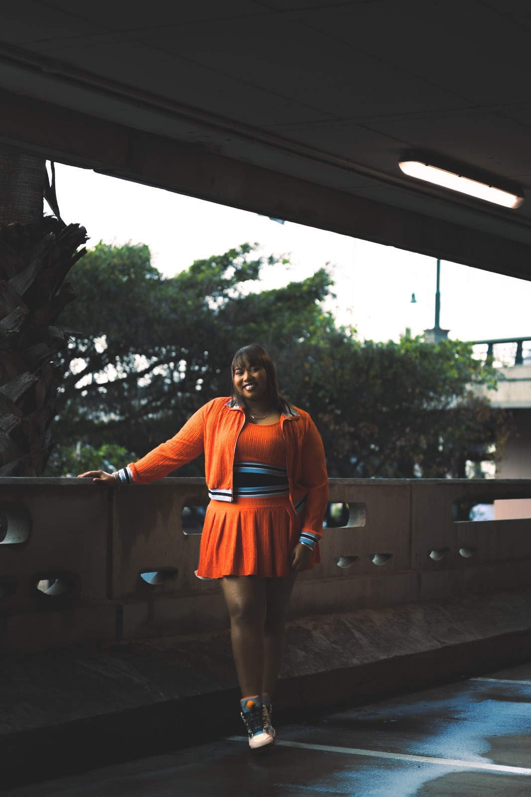 Full-length portrait of a woman in orange beside a parking-garage opening