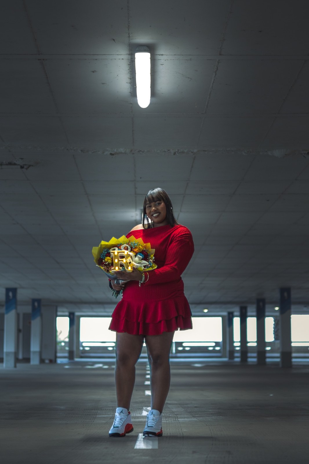Woman in a red dress holding a bright bouquet beneath a fluorescent light
