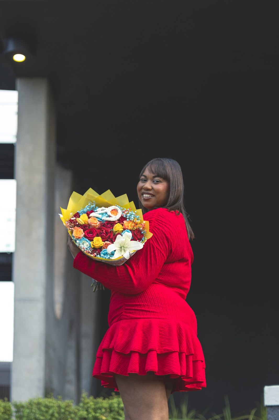 Woman looking over her shoulder while holding flowers against a dark wall