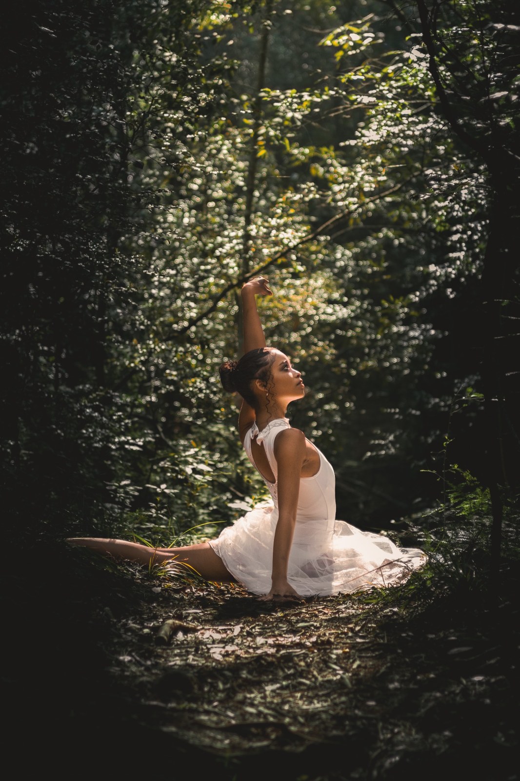 Woman seated on a mossy ledge with one arm raised toward the forest canopy