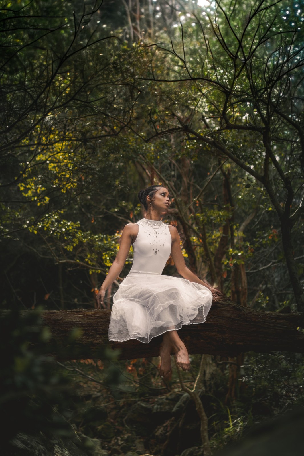 Woman perched on a fallen branch with her white skirt spread around her