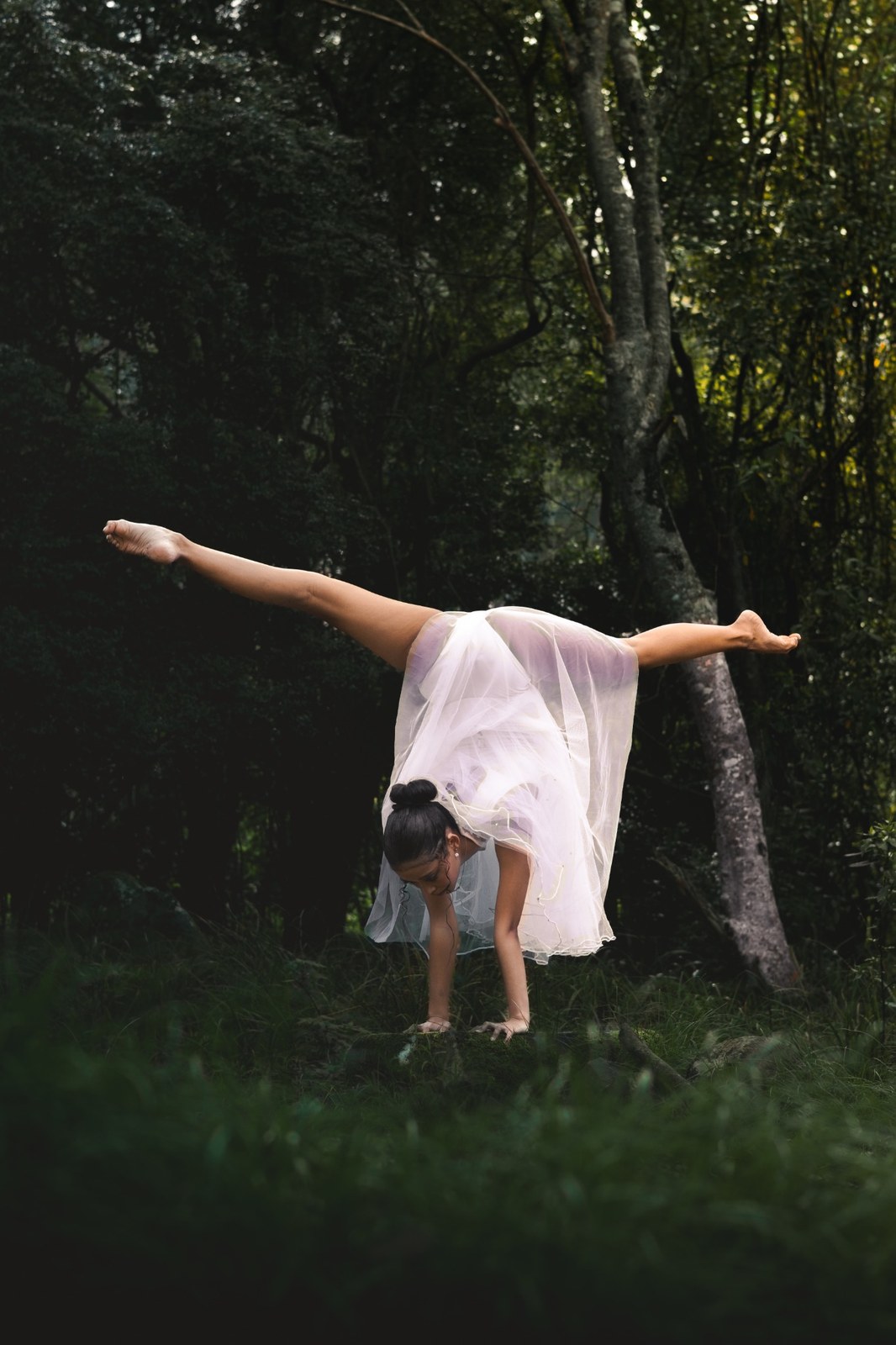 Woman balancing on her hands with legs extended among the trees