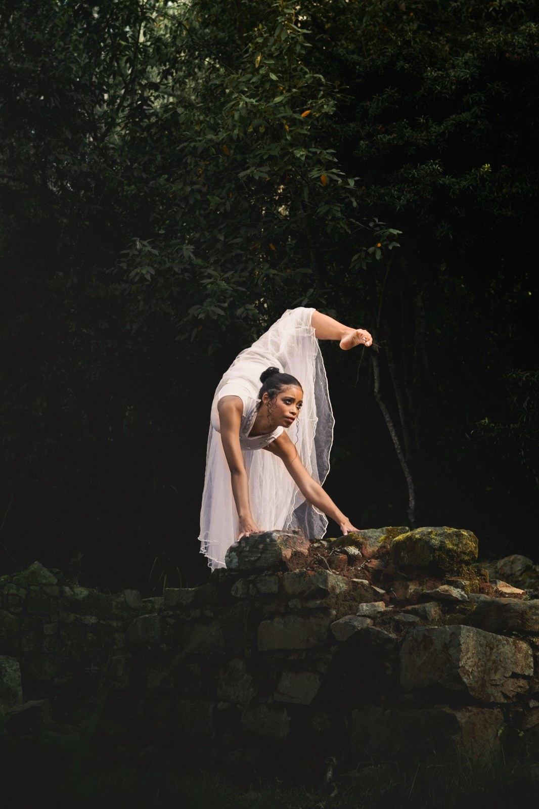 Woman bending sideways over a rocky ledge in a flowing white dress