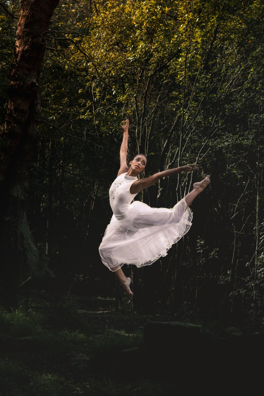 Woman captured mid-leap in a white dress against the dark forest