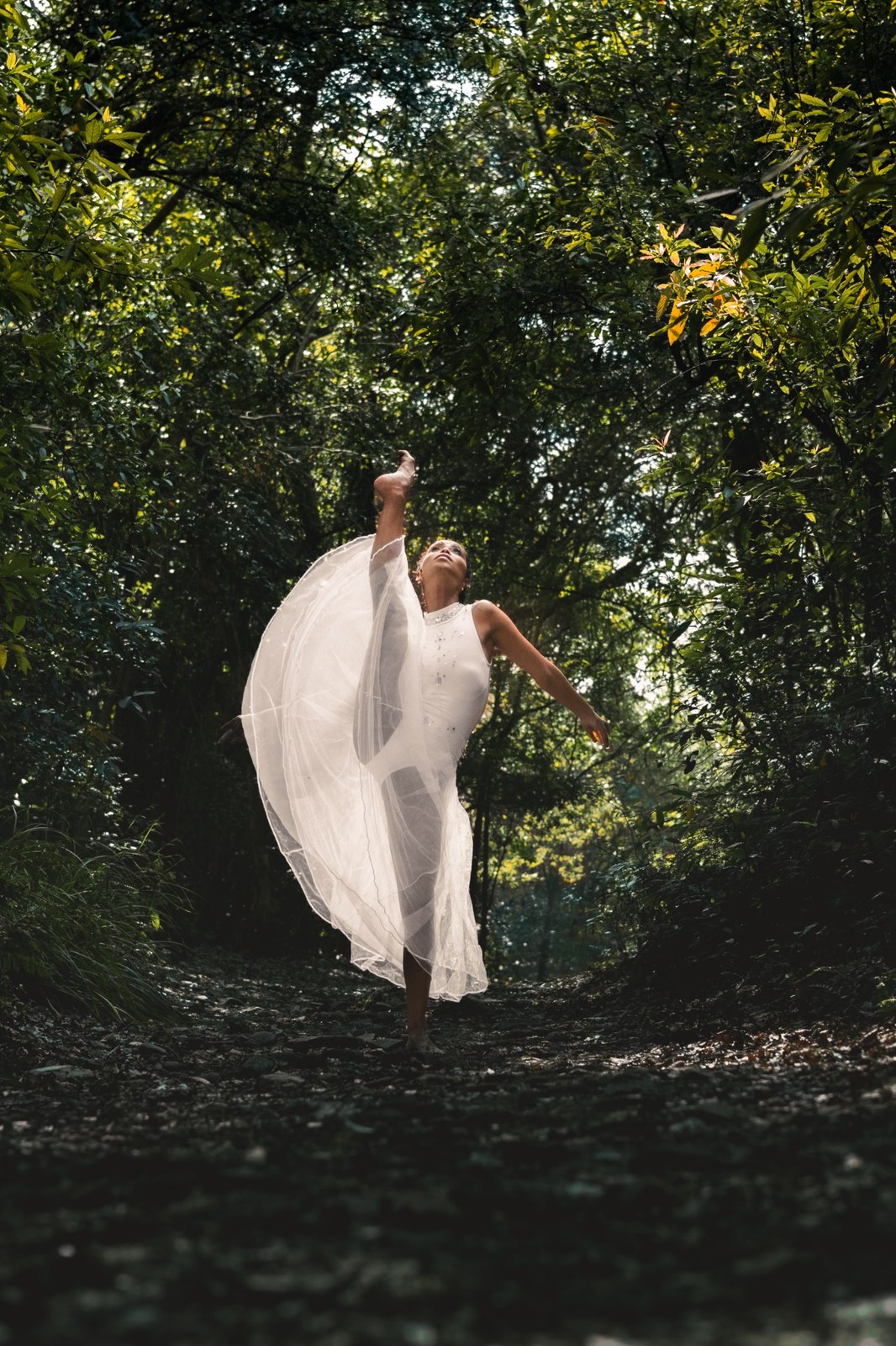 Woman turning beneath the trees with her white skirt lifted by movement