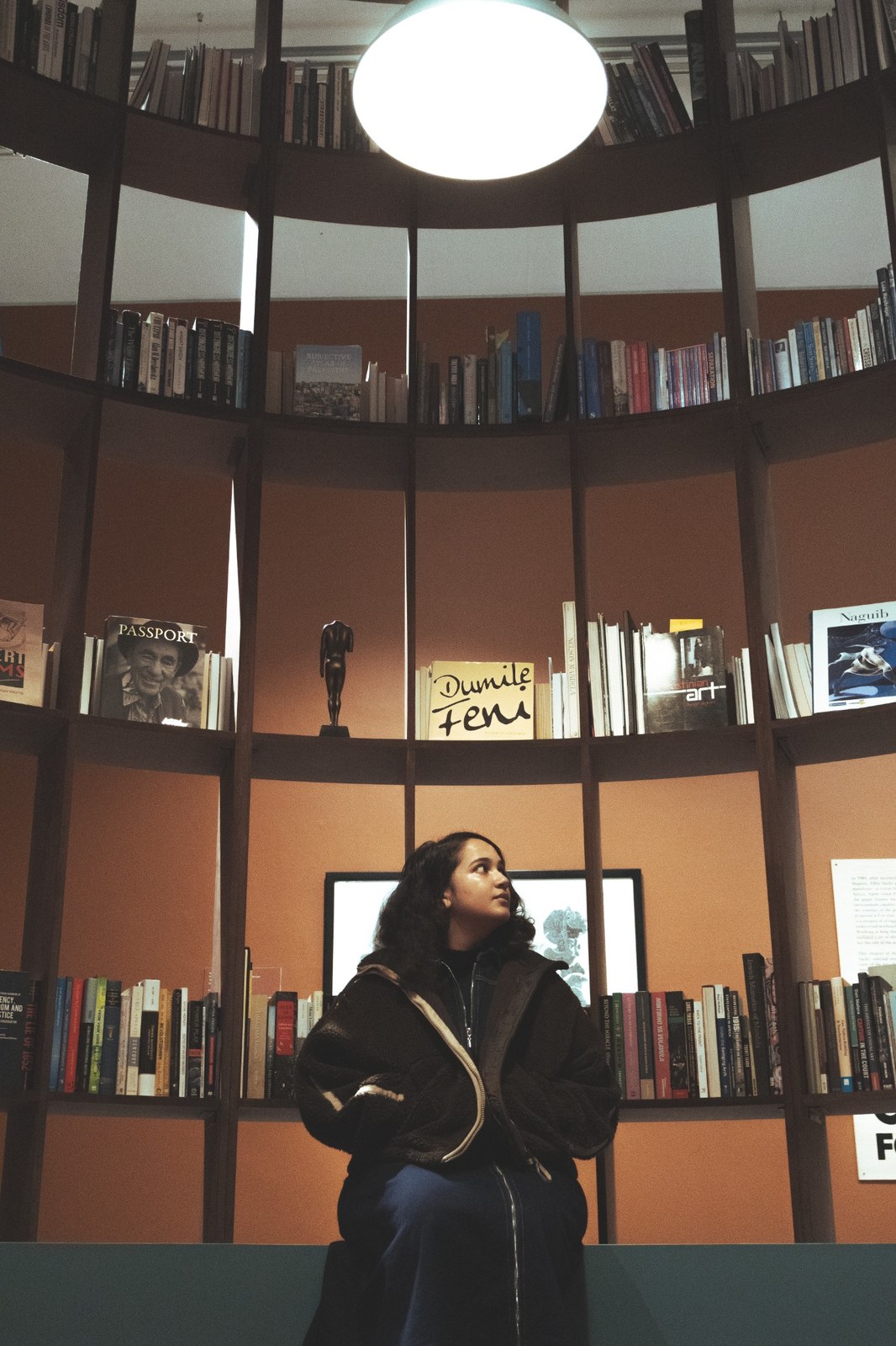 Woman beneath circular bookshelves and a hanging globe light at Zeitz MOCAA