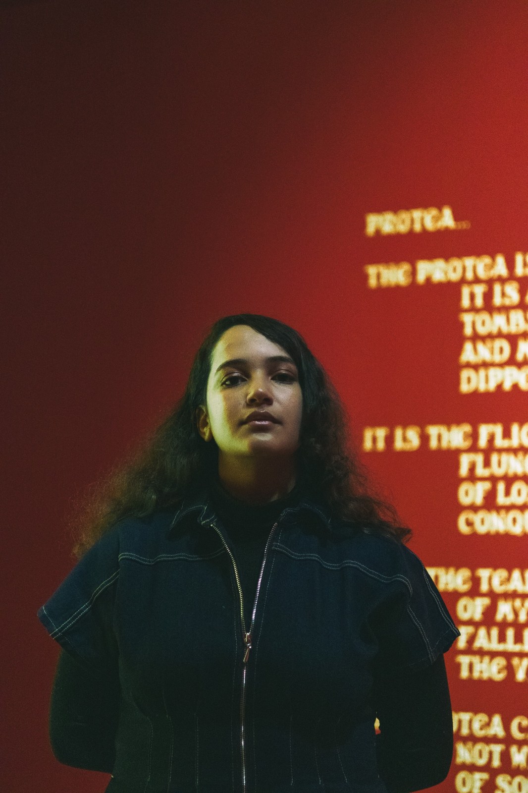 Woman standing against a red gallery wall with illuminated lettering