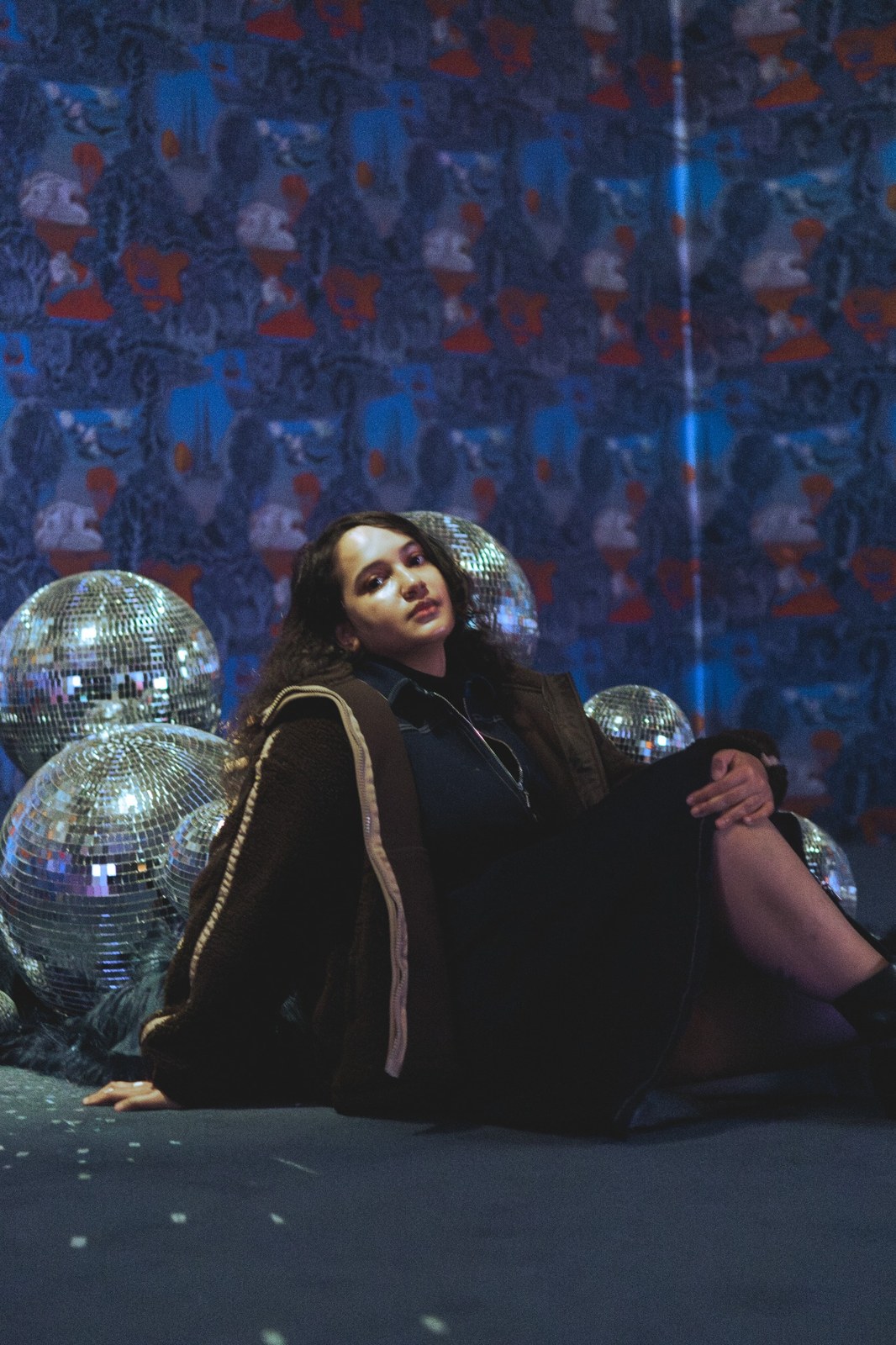 Woman seated beside mirrored disco balls in a blue-lit installation