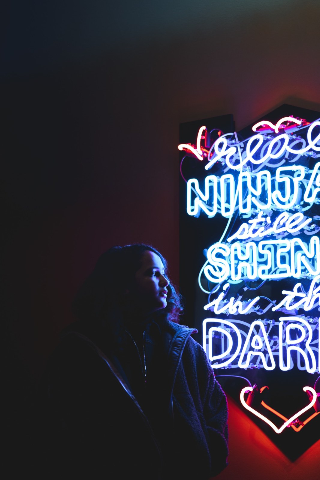 Woman lit by colourful neon writing on a dark gallery wall