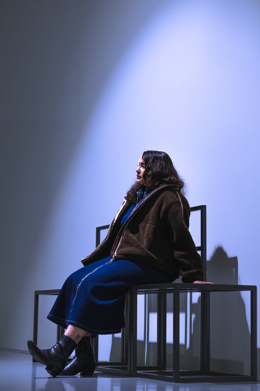 Woman seated on tall chairs beneath a pool of blue light